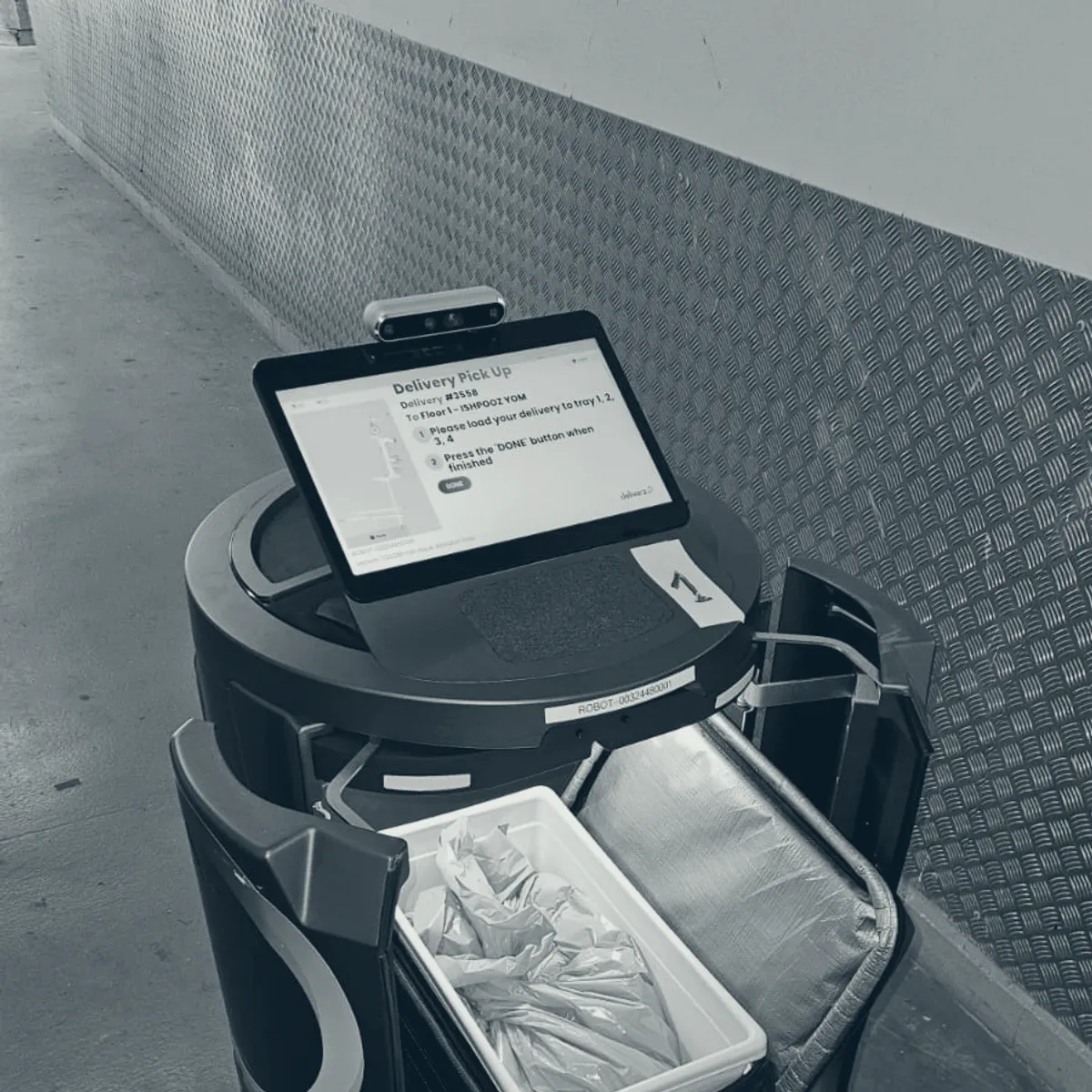 A robot loaded with sealed deliveries, its screen showing the mission it has been dispatched on.