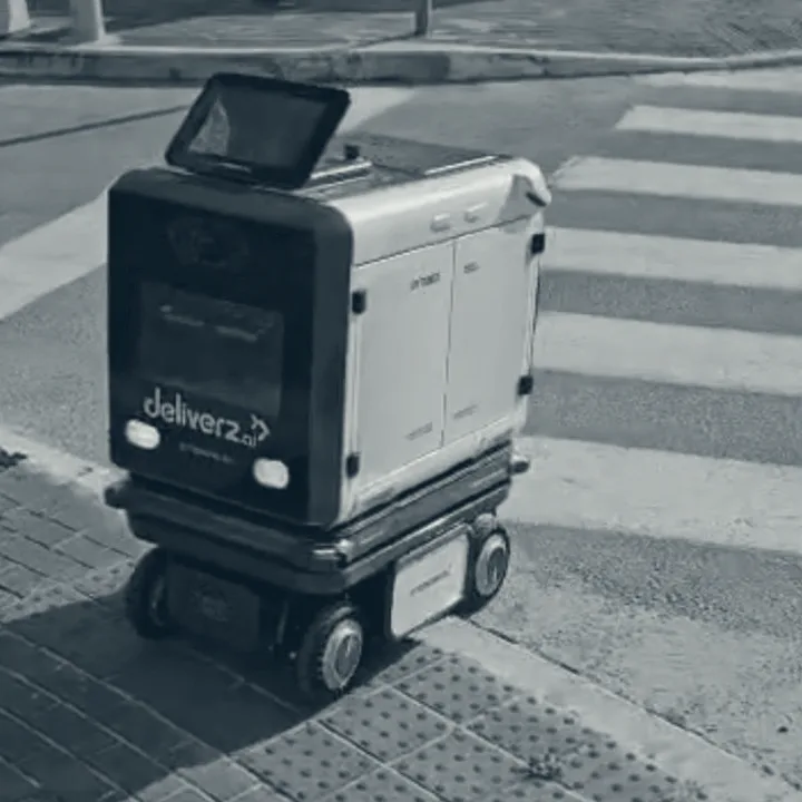 A delivery robot outdoors on a campus, crossing a road at a marked crossing.